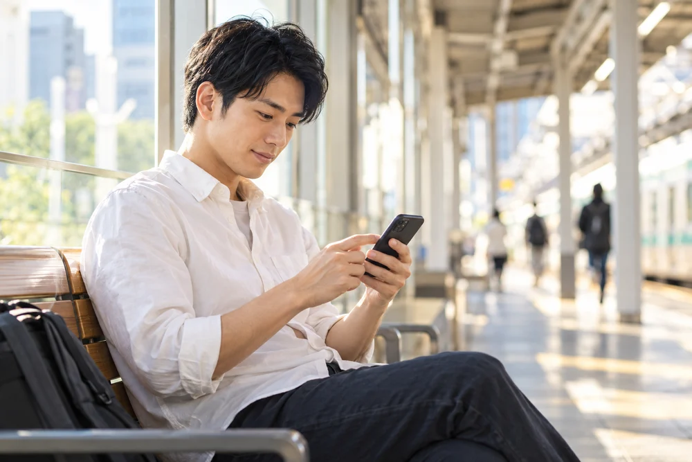 移動の合間にスマートフォンを使う男性のイメージ